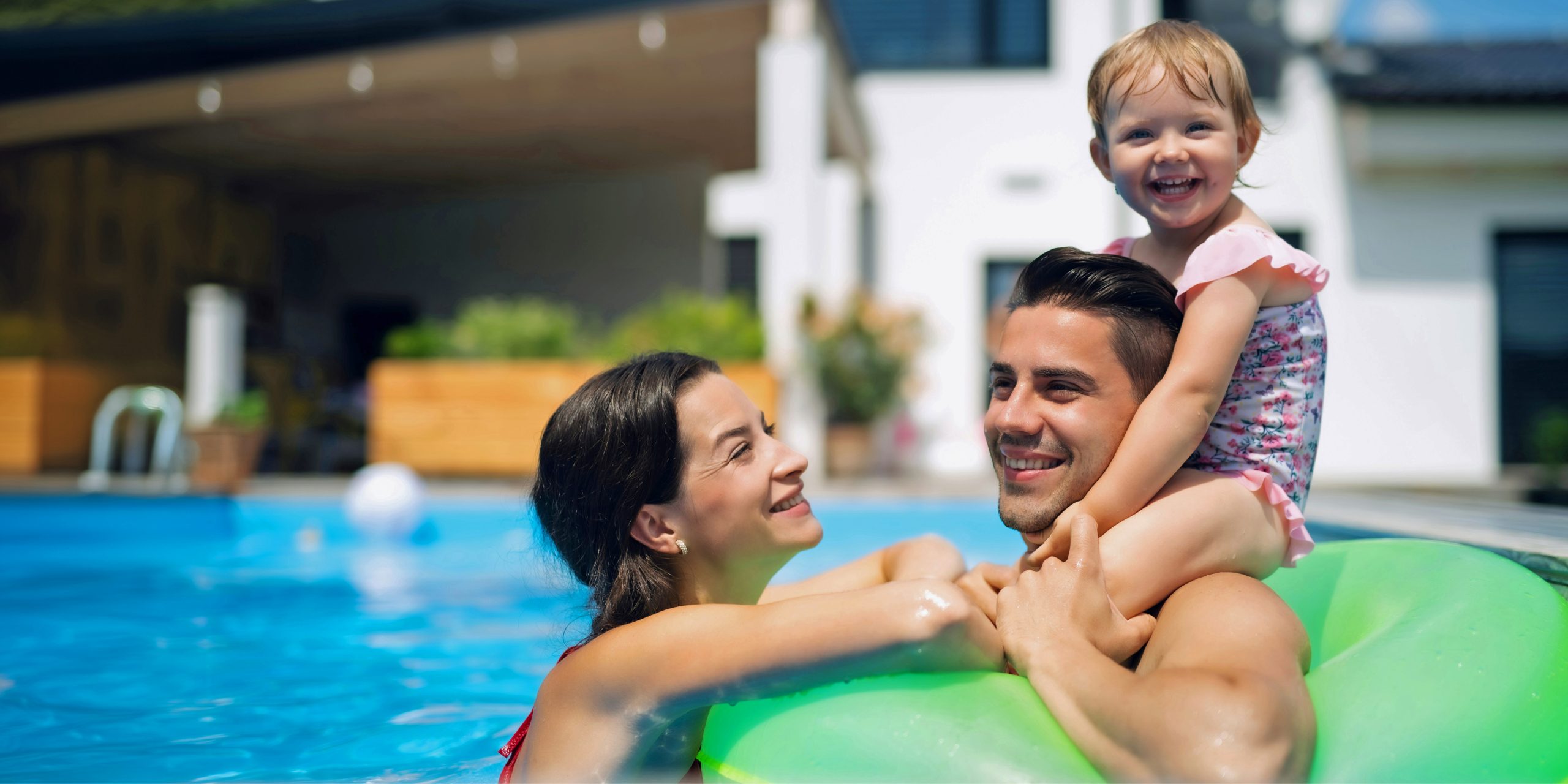 Happy woman, man and little girl swimming in a pool on a green inner tube.